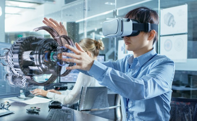 A man wearing a virtual reality headset sits at a desk and manipulates a virtual object.